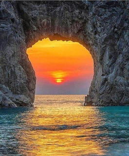 Sunset viewed through a natural rock arch over turquoise ocean water with orange and pink sky