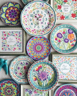 Collection of colorful decorative ceramic plates with floral and mandala patterns arranged on a gray wall