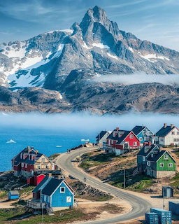 Colorful wooden houses on hillside with snow-covered mountain peak and coastal waters