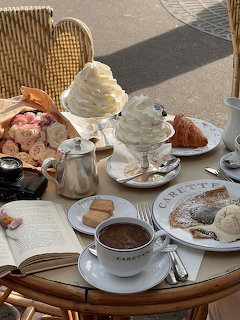 Cafe table with hot chocolate, whipped cream, pastries, and coffee in sunlight