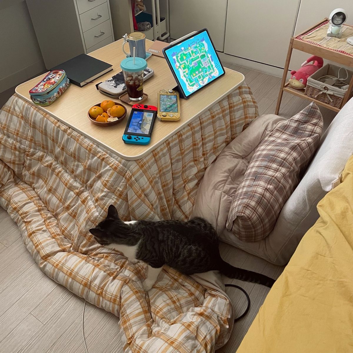 Black cat resting next to a kotatsu table with tablet and snacks in a Japanese living room