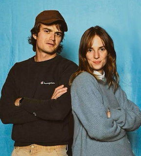 Two people in casual sweaters with crossed arms against blue background