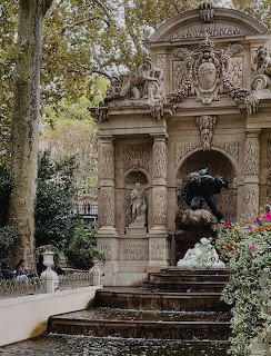 Ornate stone fountain with steps and flowers in a leafy garden