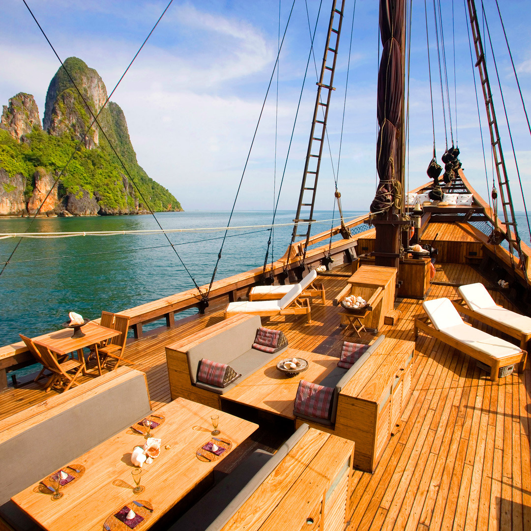 Wooden yacht deck with seating area, calm tropical sea and green island peaks in background