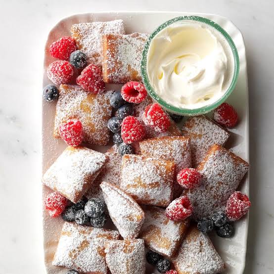 Powdered sugar-dusted pastries with fresh berries and cream on white marble