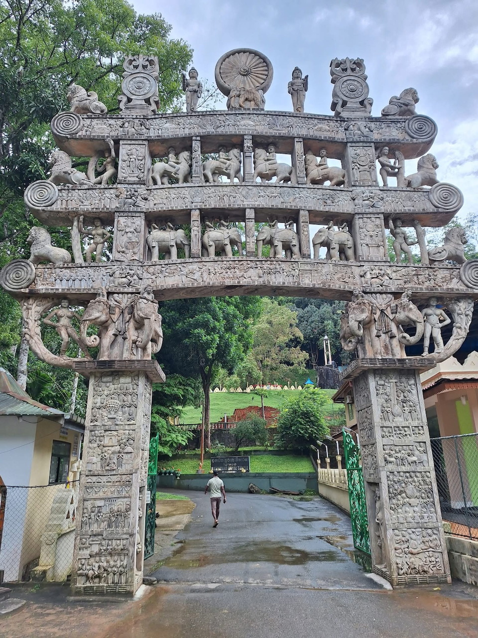 Ornate Sri Lankan stone temple gate with carved lions and multi-tiered roof under cloudy sky