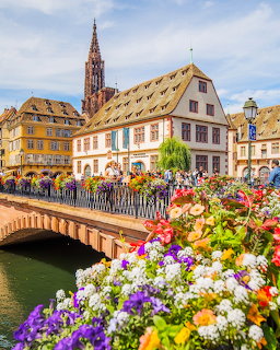 Flower-filled bridge over a canal in a historic European town with colorful buildings and a church spire