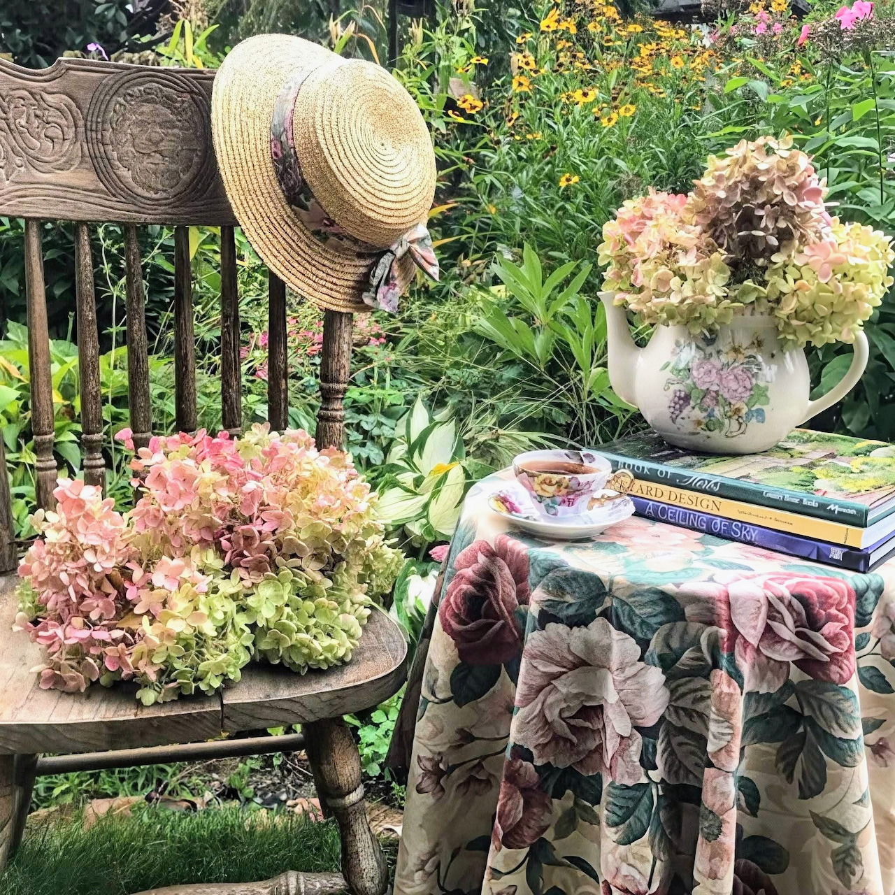 Garden table with teacup, hydrangeas, books, and straw hat among flowers