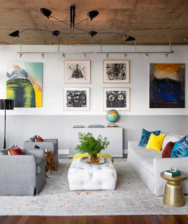 Modern living room with gray sofas, gallery wall art, white ottoman, and colorful throw pillows
