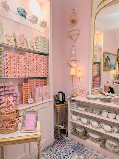 Pink café interior with shelves of macarons, white dishes, ornate mirror, and pastel décor