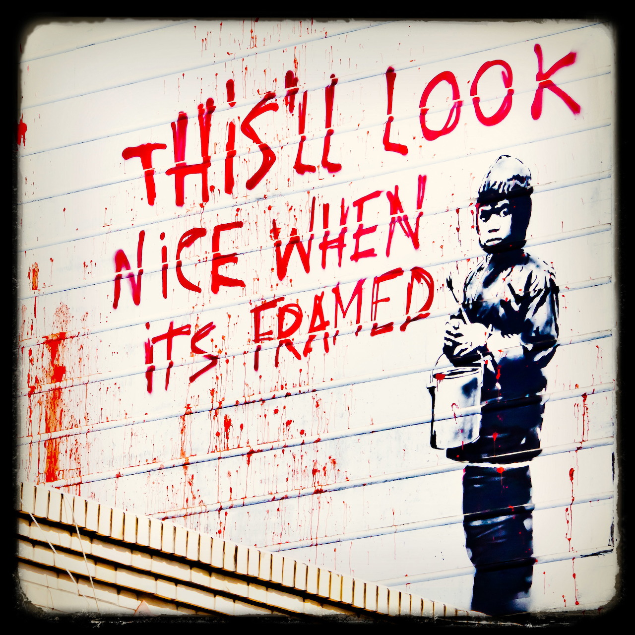 Red graffiti text and a stencil child holding a paint bucket on a white wall