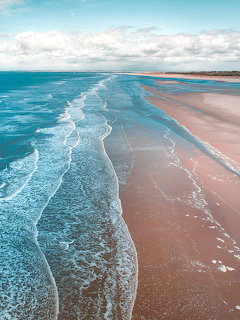 Gentle ocean waves along a wide sandy beach under a cloudy sky