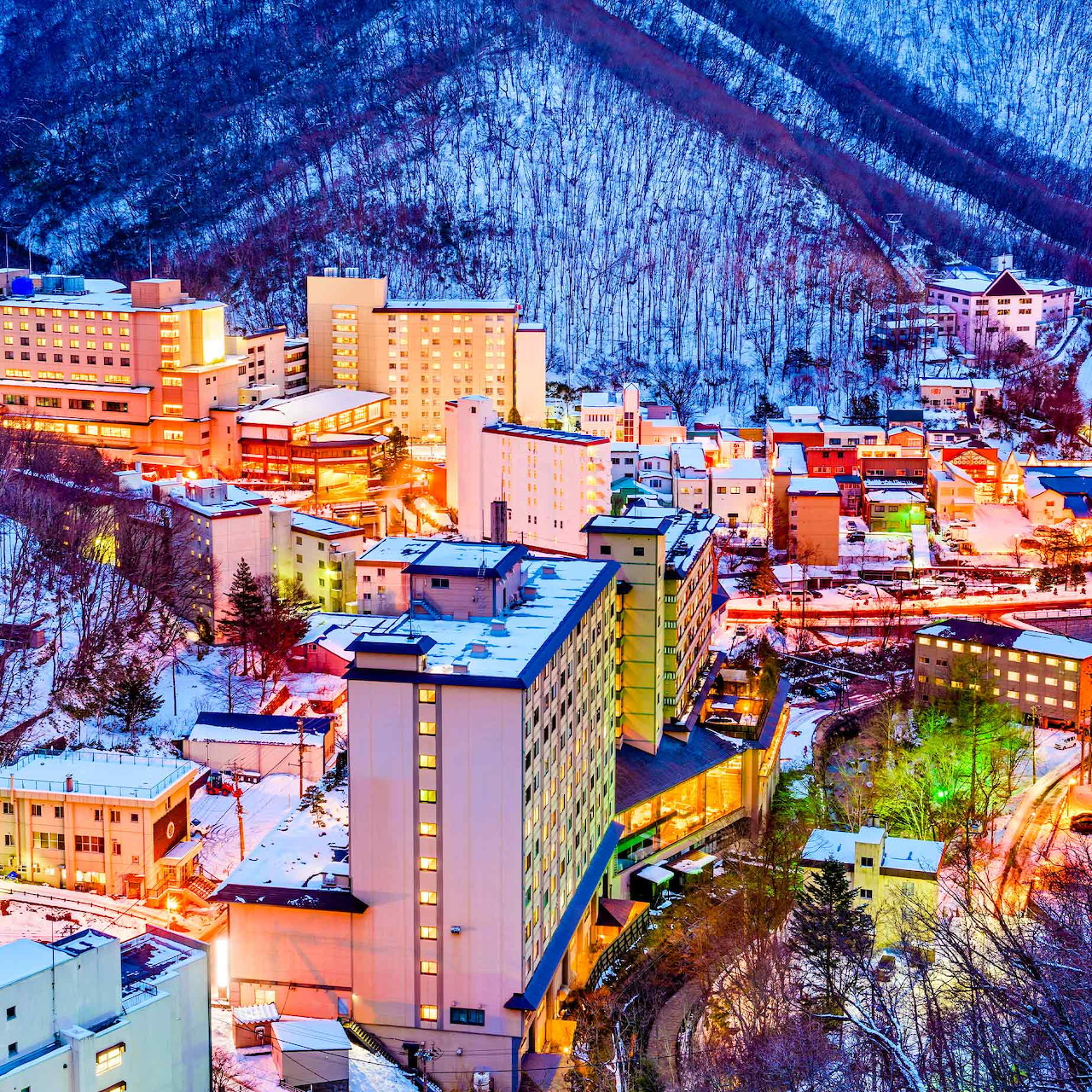 Aerial view of lit buildings in snowy mountain valley at dusk