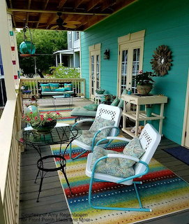 Covered porch with turquoise walls, white wicker furniture, and vibrant multicolored striped rug
