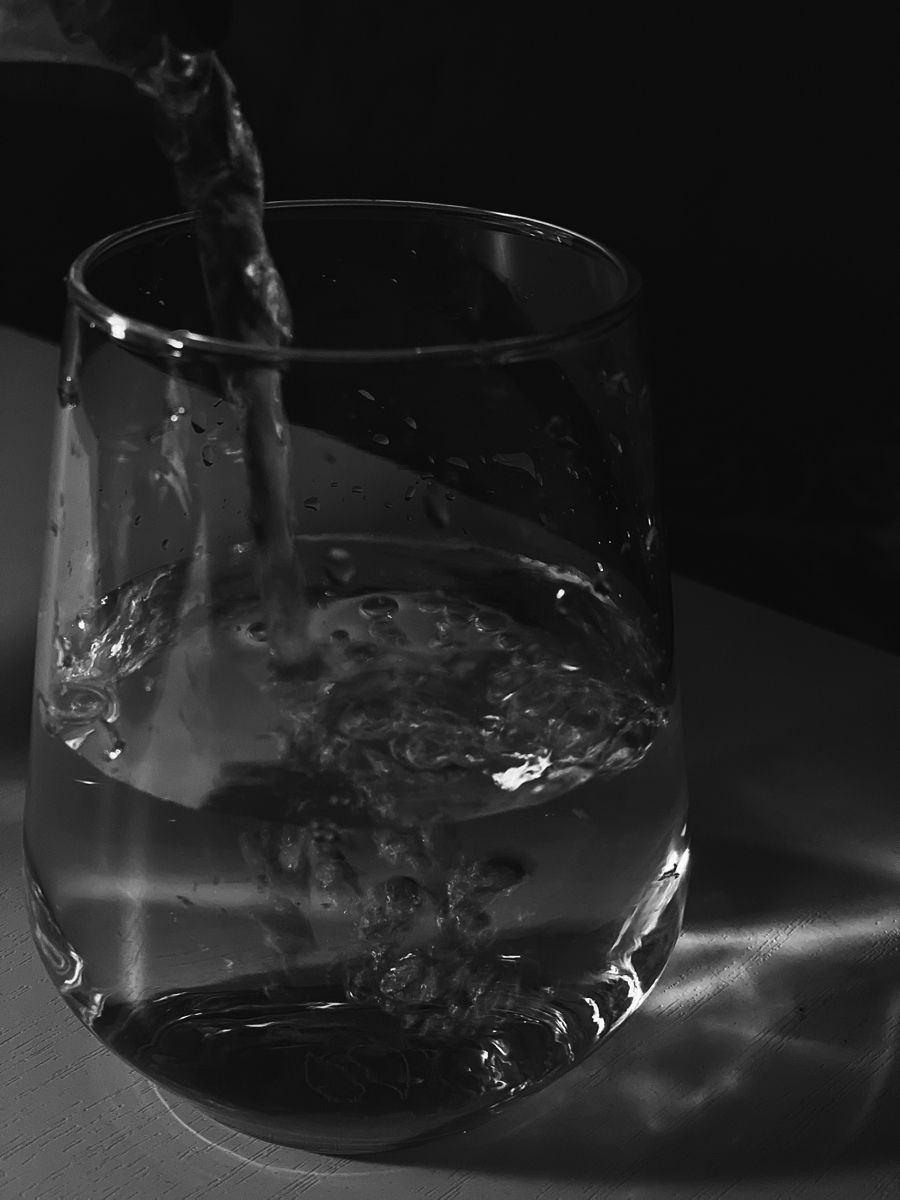 Clear glass with water being poured in against a black background