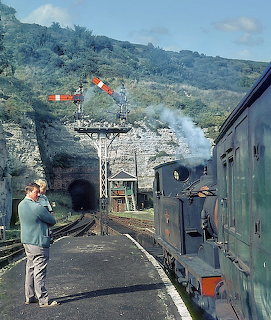 Steam locomotive W26 at Ventnor station platform with photographer and mountain backdrop, 1965