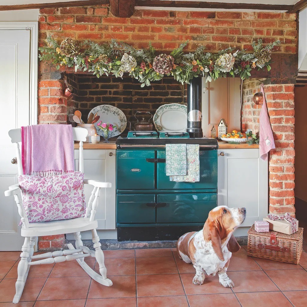 Rustic country kitchen with teal stove, brick walls, rocking chair, and dried flowers