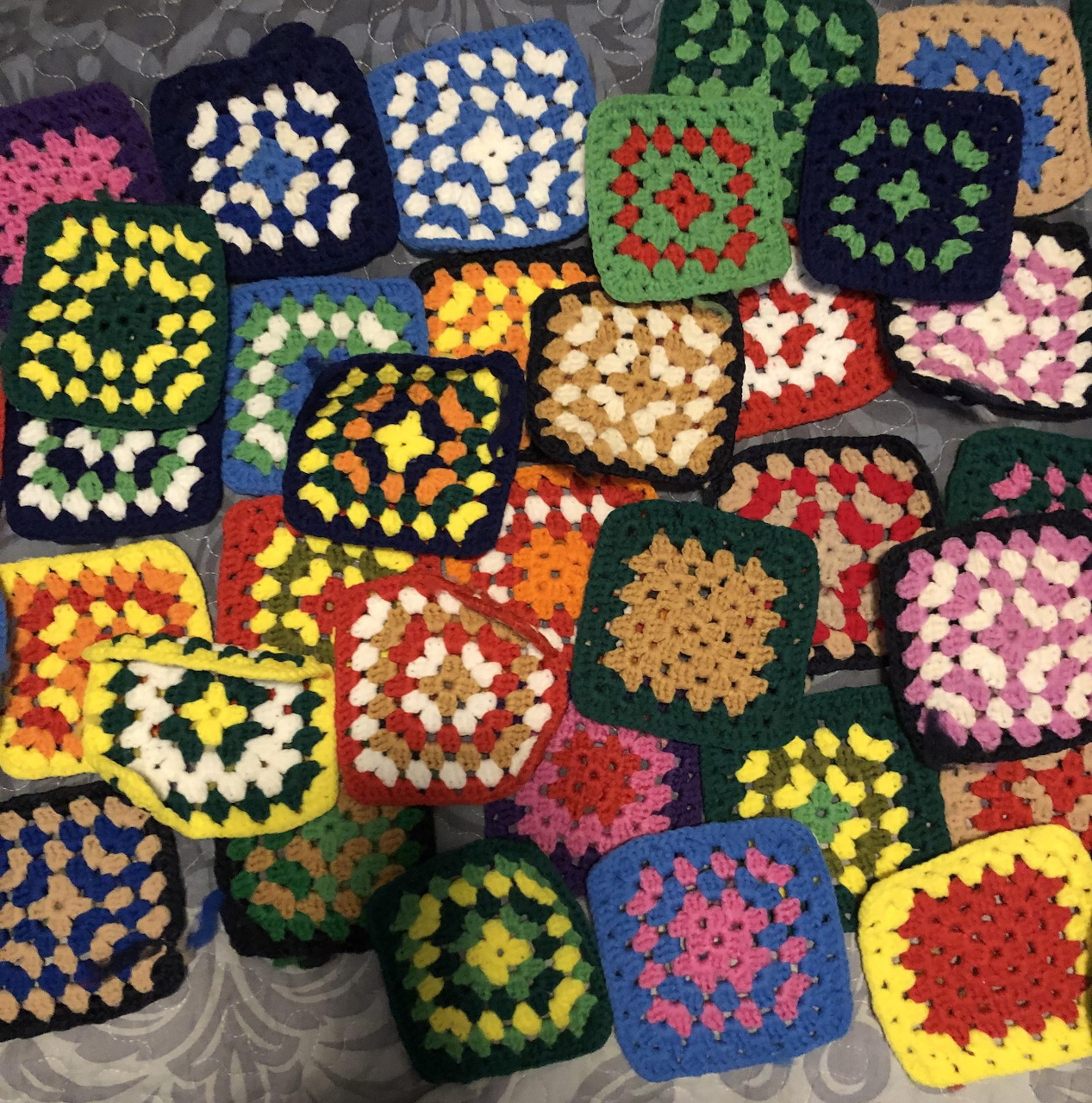 Pile of multicolored crochet granny squares with black borders in various bright yarn colors