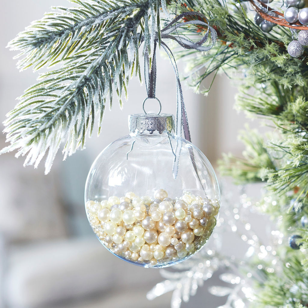 Glass globe ornament filled with pearl beads hanging on a frosted Christmas tree branch