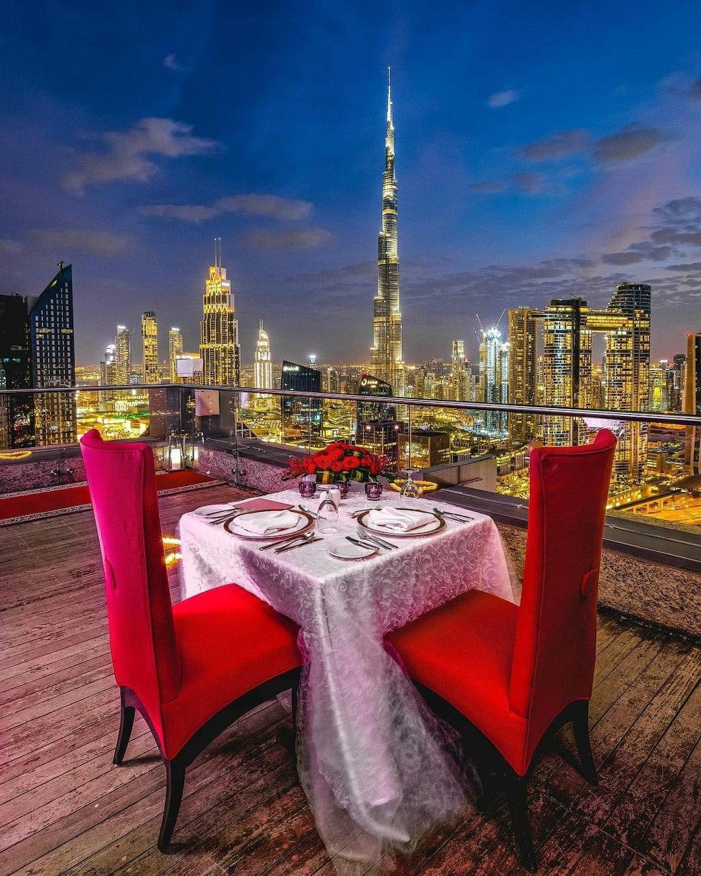 Elegant dinner table for two with red chairs on rooftop terrace overlooking Dubai skyline at night
