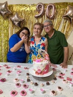 Three people smiling behind a 90th birthday cake with gold and silver balloons in the background