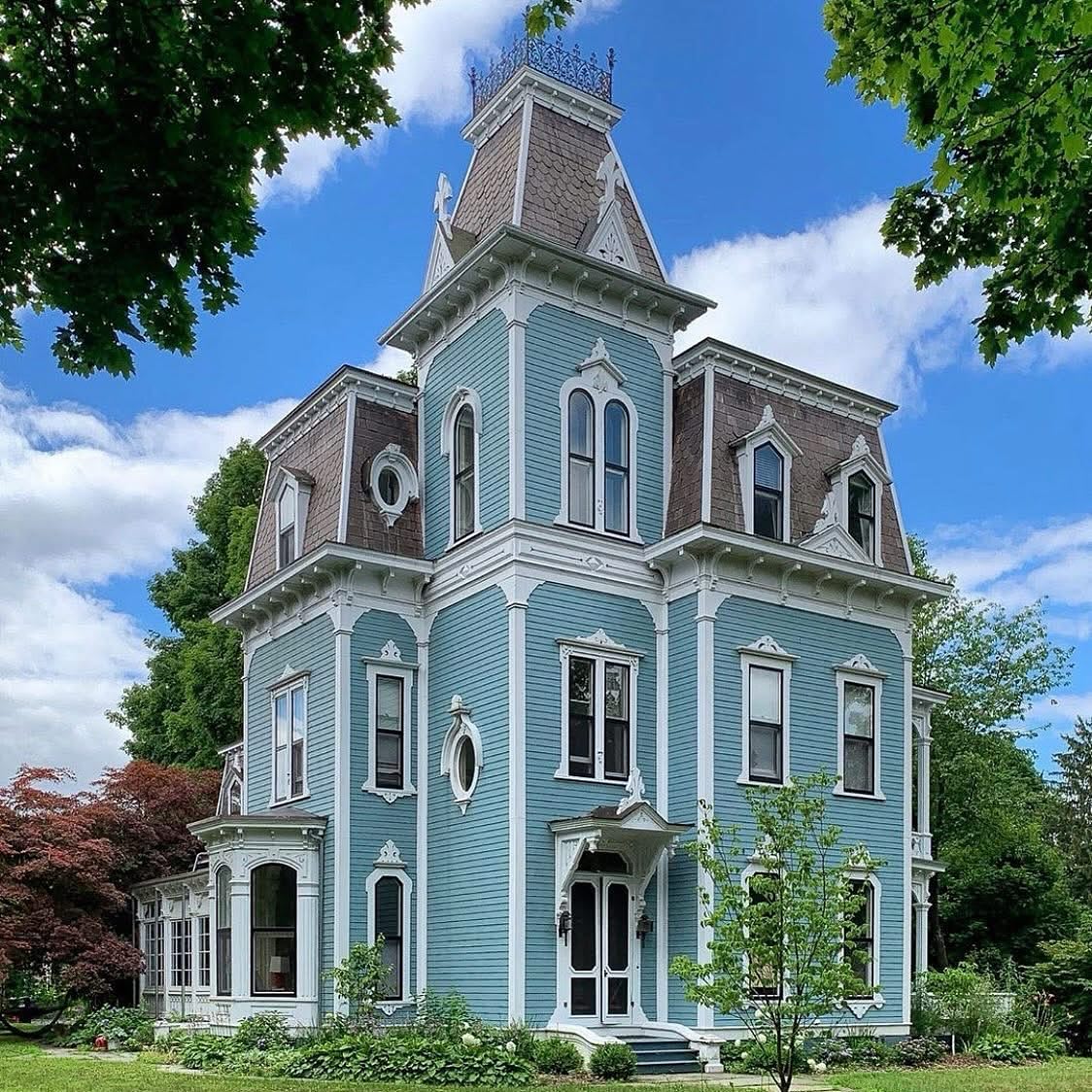 Light blue Victorian house with decorative tower and white trim on green lawn