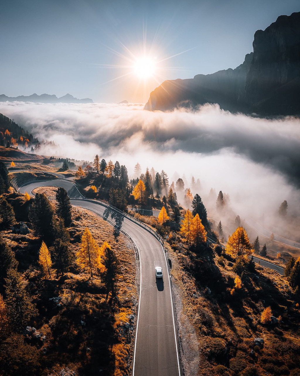 Aerial view of a winding road through golden autumn larch trees in the Dolomites with fog and sunrise