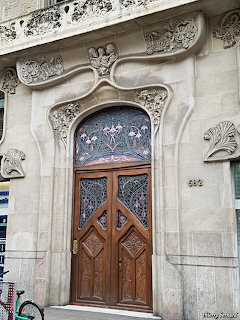 Ornate Art Nouveau doorway with carved stone facade, stained glass transom, and wooden double doors