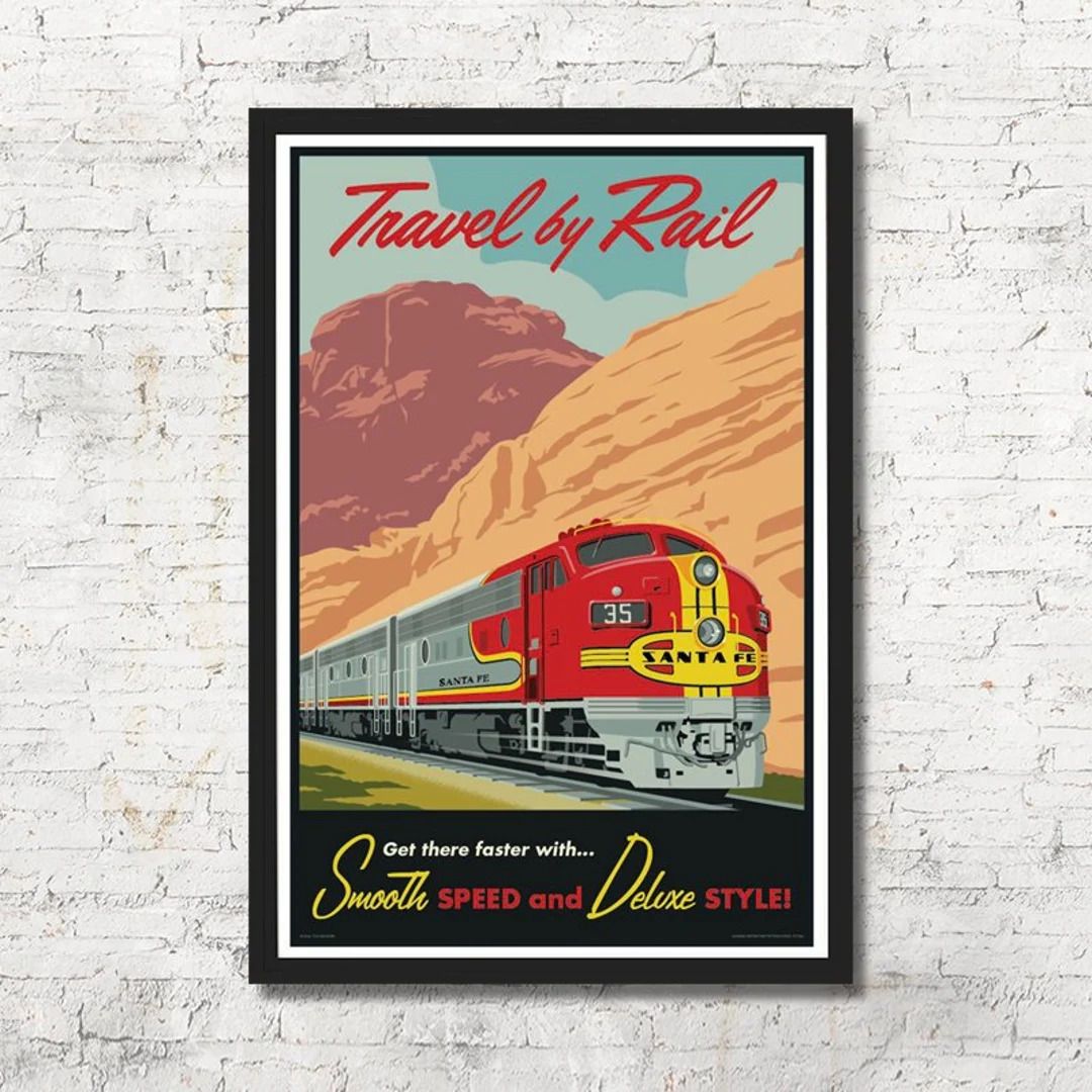 Framed vintage travel poster of a red train passing mountains on a white brick wall