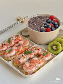 Shrimp spring rolls on a white tray with chopsticks, a purple smoothie bowl with beries, and sliced kiwi