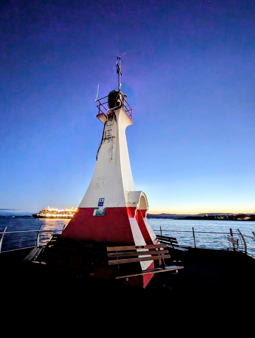 White and red lighthouse beside calm water at dusk with a clear blue sky