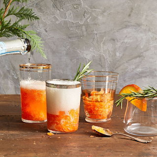 Three cocktail drinks in glasses on a wooden table with citrus garnish and herbs