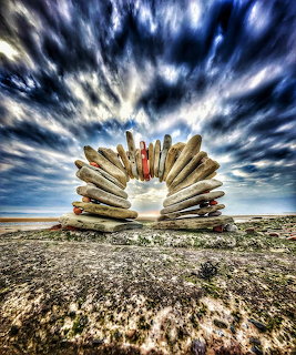 Driftwood arch on a rocky beach under a dramatic cloudy sky