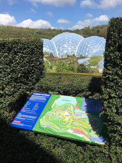 Visitor map sign at Eden Project with large geodesic biome domes and green hills in background, Cornwall