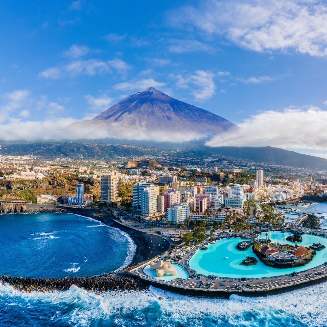 Coastal city with seaside pools, a bay, and a large mountain in the background