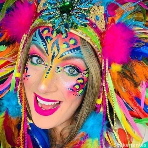 Smiling woman with colorful neon carnival face paint, feathered headdress, and glitering accessories