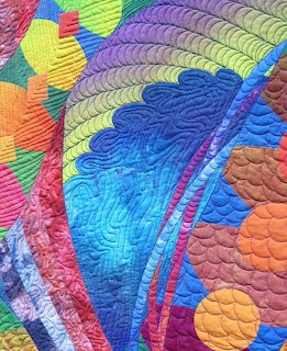 Close-up of colorful quilted fabric with curved geometric patterns and intricate stitching in blues, greens, and warm tones