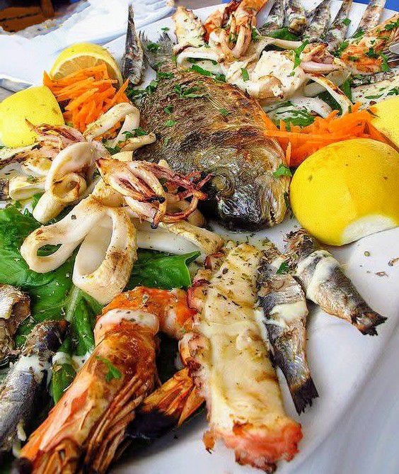 Grilled seafood platter with fish, prawns, squid and lemon on white plate