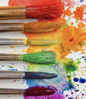 Rainbow-colored paintbrushes with corresponding paint streaks and splatters arranged on white background