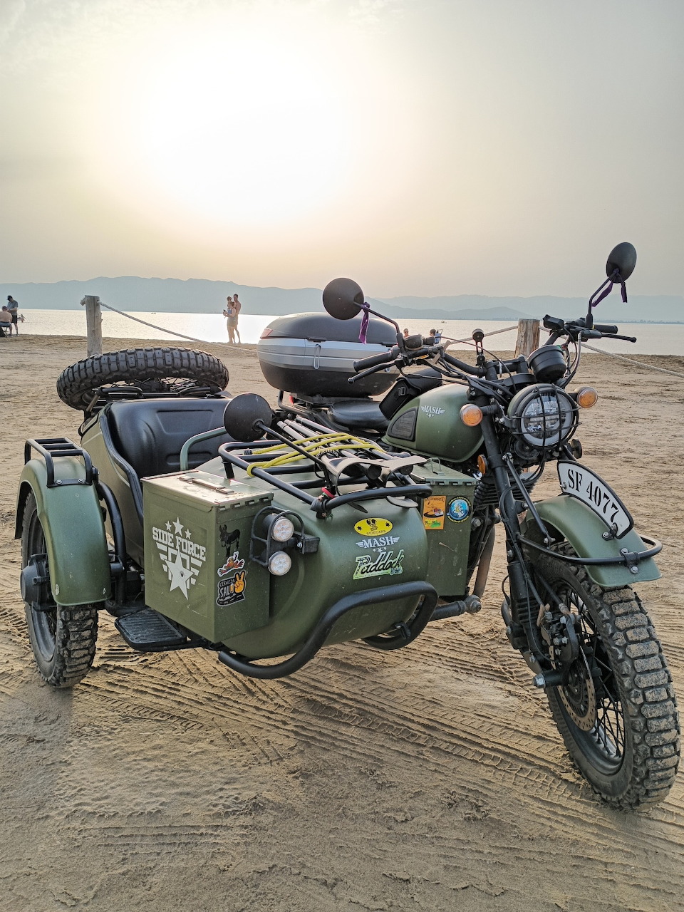Vintage green motorcycle with sidecar parked on a sandy beach at sunset