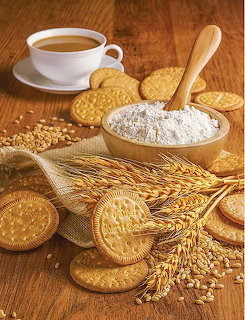 Round cookies with flour in wooden spoon, wheat stalks and coffee cup on wooden table
