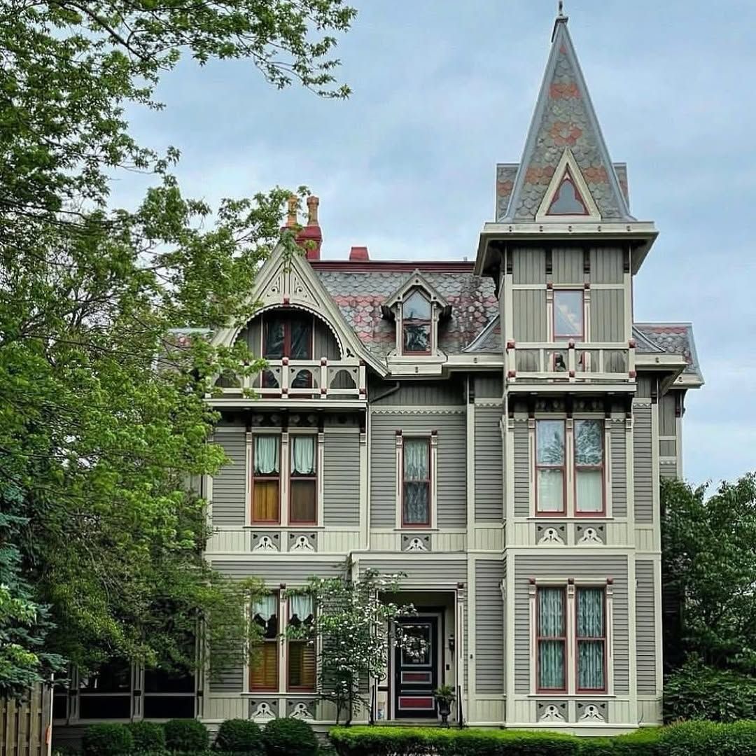 Gray Victorian house with tower and decorative trim surrounded by trees