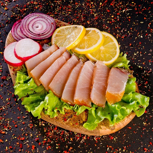 Circular platter of sliced ham garnished with lettuce, lemon slices, radish, and red onion on dark speckled counter