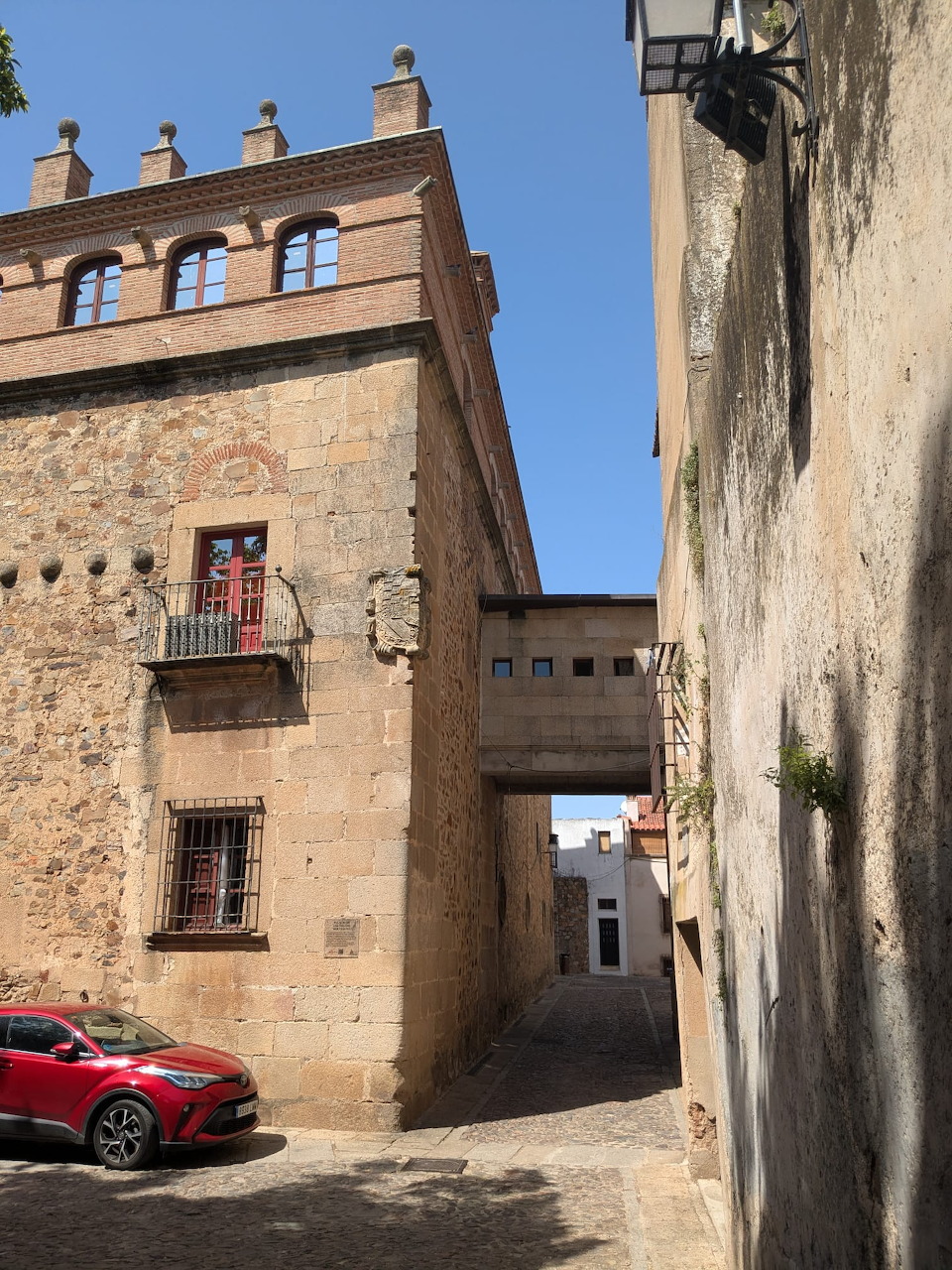 Historic stone street in Caceres with old buildings, an overhead passage, and a red car