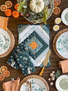 Overhead view of an autumn-themed table setting with quilted napkins, botanical plates, pumpkins, and dried oranges