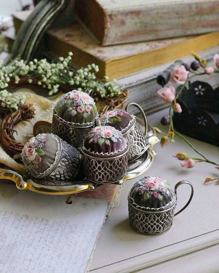 Vintage embroidered pin cushions in silver filigree holders arranged on a gold tray with dried flowers