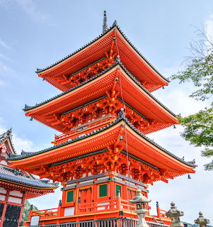 Red three-story Japanese pagoda with traditional tiered roofs and ornate details against blue sky