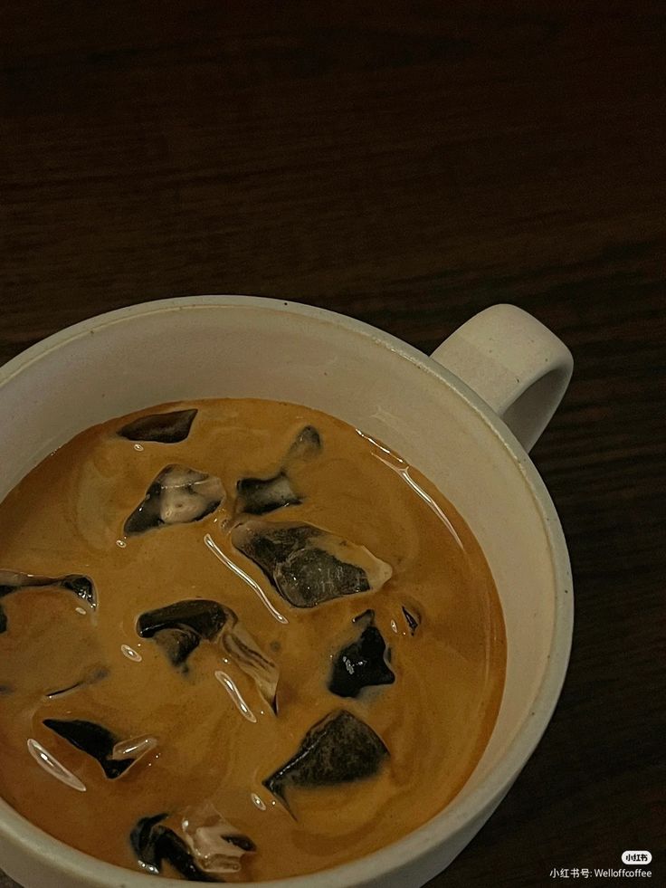 Iced coffee with ice cubes in white mug on dark wood table