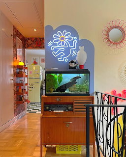 Eclectic colorful interior with fish aquarium on retro cabinet, blue wall mural of cat and flower, and vintage decor