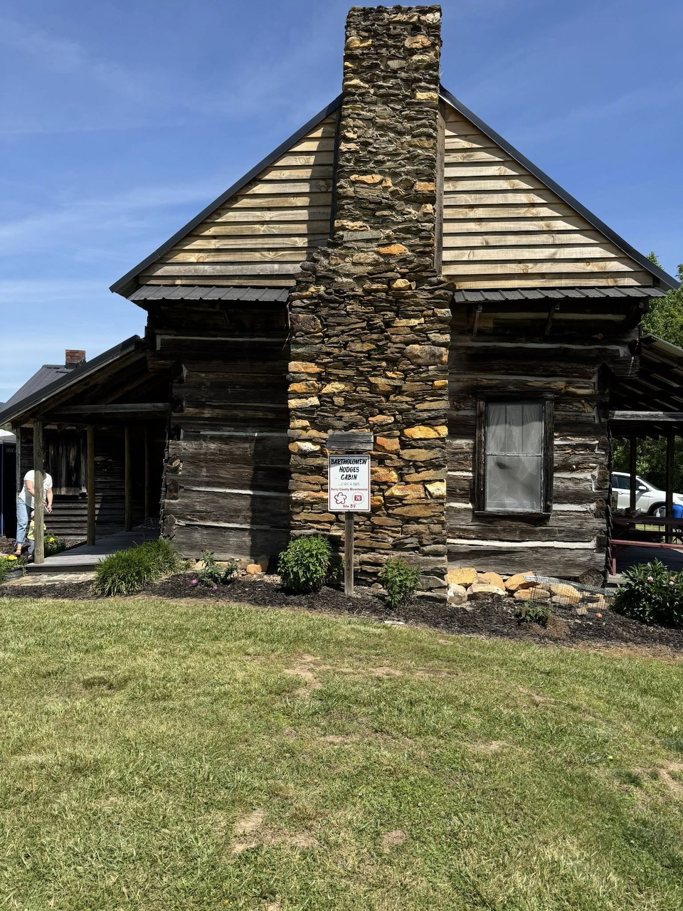 Old log cabin with a stone chimney and grassy lawn under a blue sky